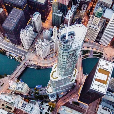 Aerial view of a cityscape with a prominent modern skyscraper near a river, surrounded by other tall buildings and intersecting roads.
