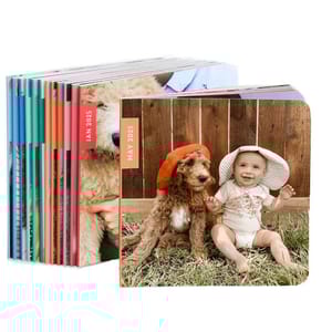 Stack of customized photo books showing a cover with a baby and a dog wearing hats, dated May 2025.
