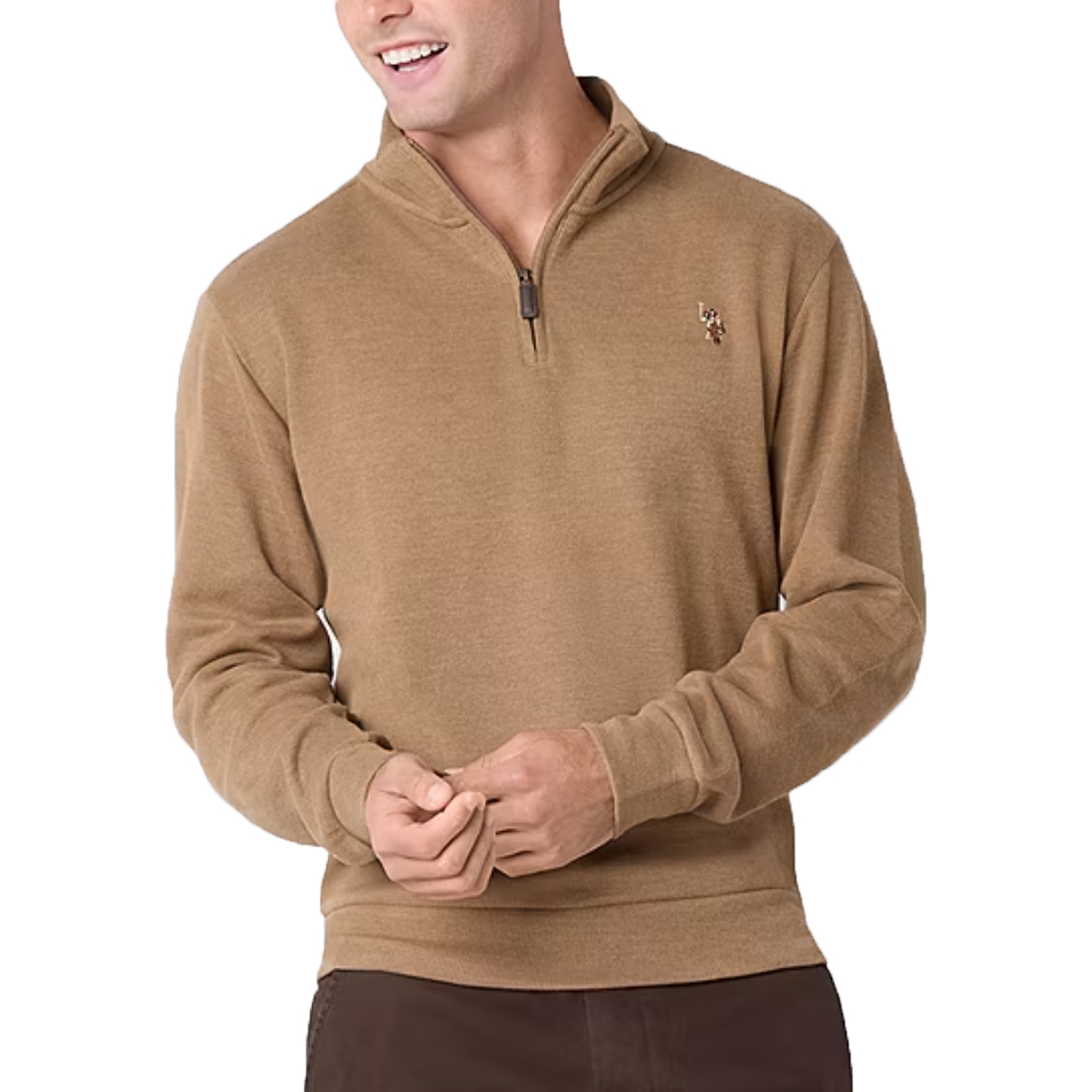 A man wears a tan quarter-zip pullover sweater with a small embroidered logo on the chest, paired with brown pants.