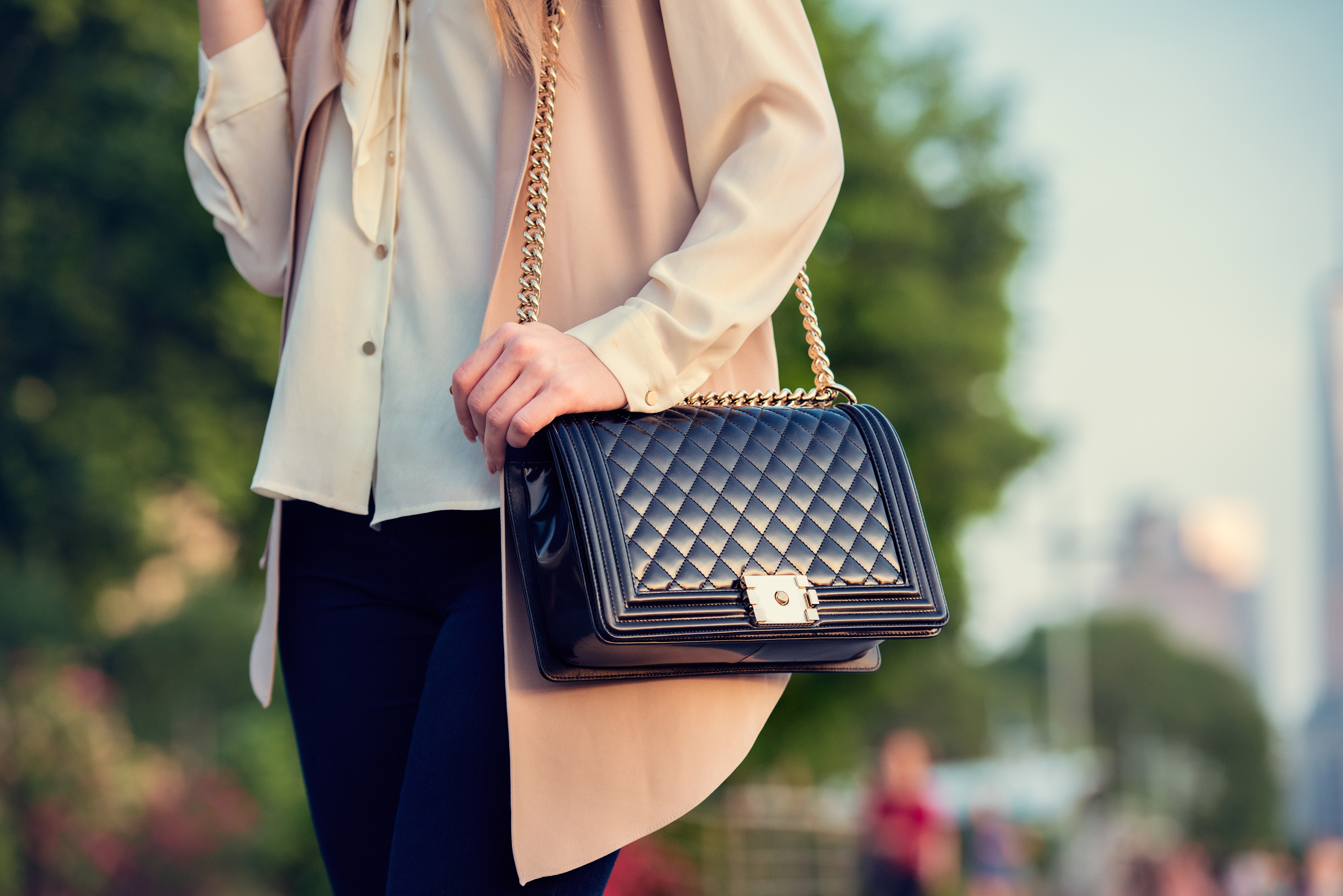 A person is holding a black quilted shoulder bag with a chain strap.