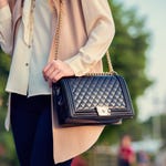 A person is holding a black quilted shoulder bag with a chain strap.