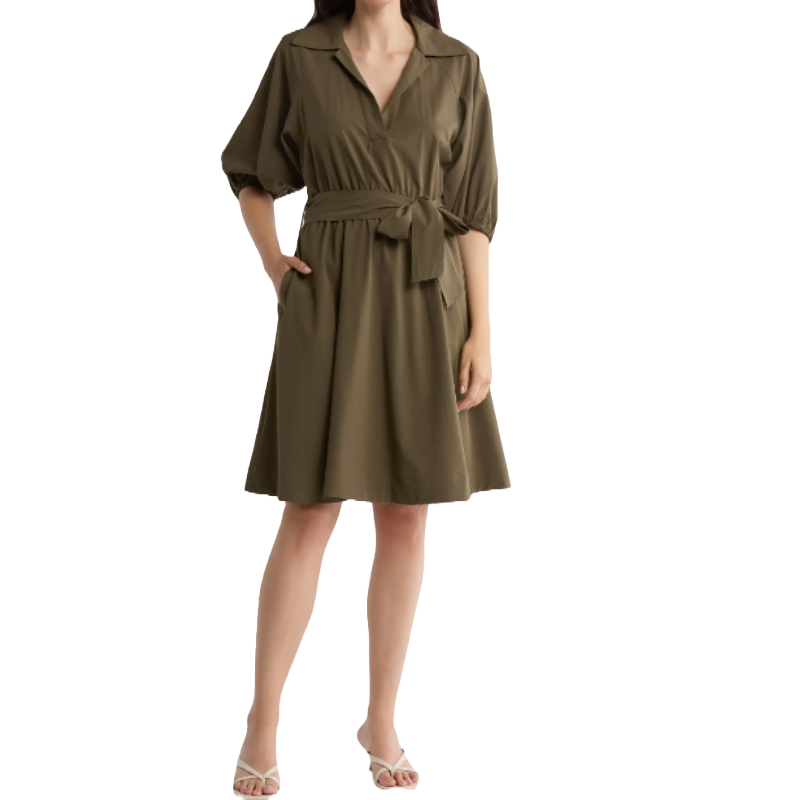 A knee-length, short-sleeve, olive-green dress with a notched collar, tie belt, and pockets. The dress has a relaxed fit and is paired with strappy sandals.