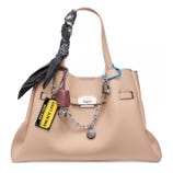 A beige DKNY handbag adorned with a black paisley scarf, silver chain, blue carabiner, and various tags including a yellow New York 1989 tag.