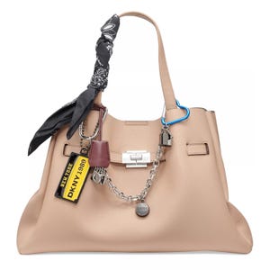 A beige DKNY handbag adorned with a black paisley scarf, silver chain, blue carabiner, and various tags including a yellow New York 1989 tag.