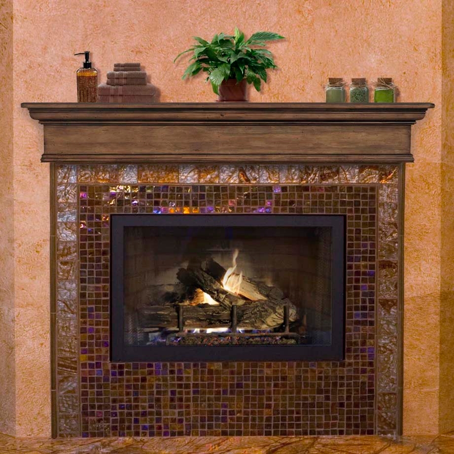 A fireplace with a wooden mantel, adorned with mosaic tiles, showcasing a lush green plant, a soap dispenser, stack of towels, and three small jars.