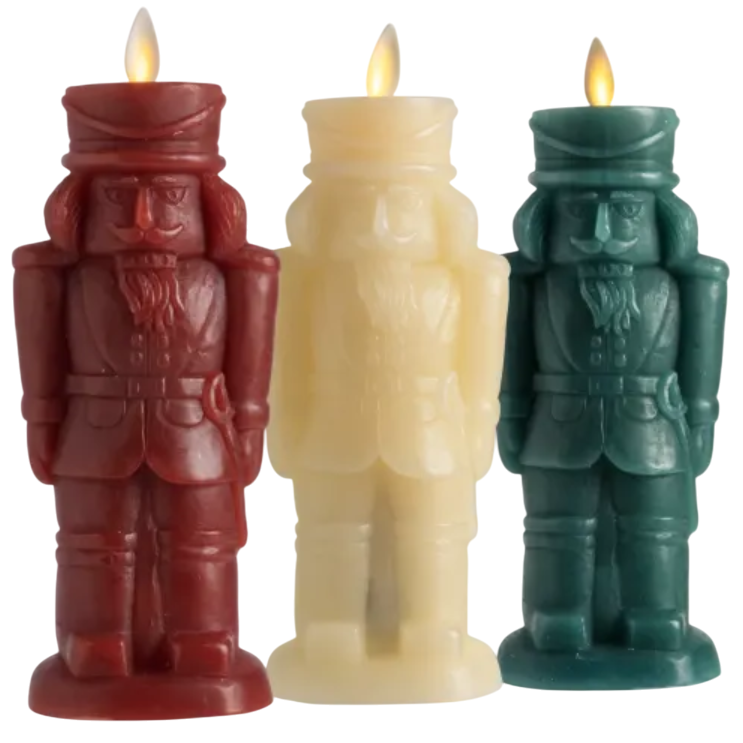 Three nutcracker-shaped candles in red, white, and green, each with a lit flame.