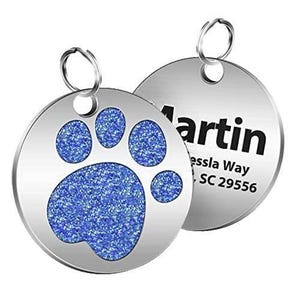 A round pet ID tag with a blue glittery paw print on one side and personalized information with a name and address on the other.