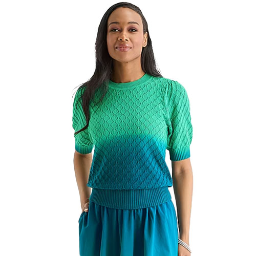 A woman is wearing a short-sleeve knit top with a braided pattern in a gradient from green to blue, paired with a matching blue skirt.