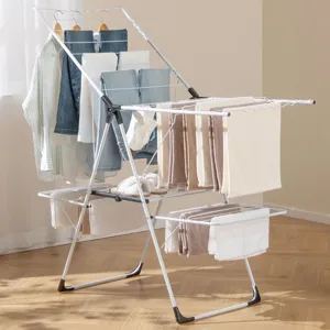 A white metal drying rack holds various clothes and towels in a well-lit room. Nearby, a grey laundry basket with handles contains a folded cloth.