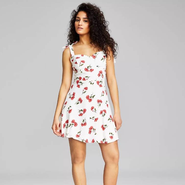 A woman is wearing a white floral dress with red flower patterns.