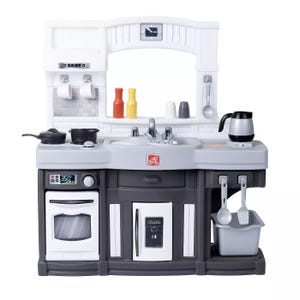Step2 Modern Kitchen is a child-sized playset featuring a stove, oven, and sink with various accessories like pots, utensils, and condiment bottles. It includes a fridge and a coffee pot, with hooks for hanging utensils and a small bin for storage.