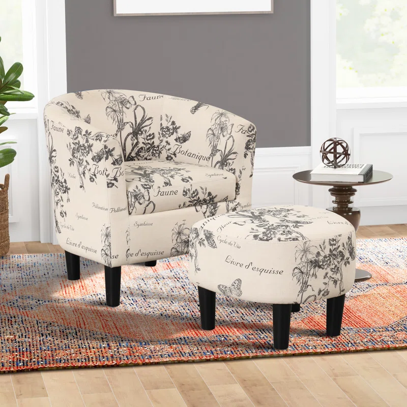 A beige botanical print armchair and matching ottoman on a multicolored woven rug, with a round wooden side table beside it.