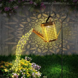 A decorative watering can light with intricate cut-out patterns projects light onto a wall and gives the appearance of pouring light onto flowers below.