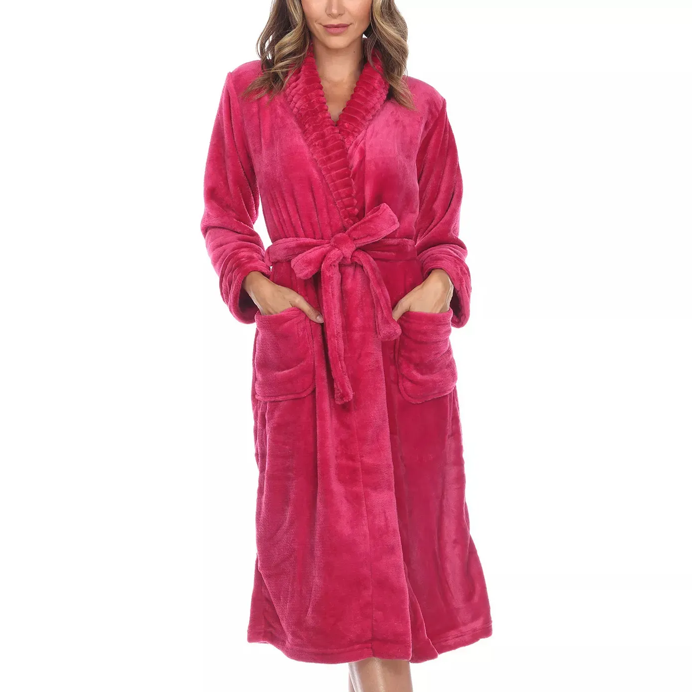 A woman is wearing a plush pink bathrobe with a shawl collar and a tied waist belt. The robe features two large front pockets.