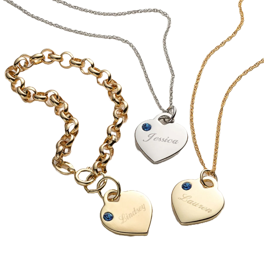 Three heart-shaped charms on necklaces feature engraved names (\“Jessica,\“ \“Lindsey,\“ \“Lauren\“), each adorned with a small blue birthstone. Chains vary in style: silver chain for Jessica, thicker gold link for Lindsey, and a thin gold chain for Lauren.