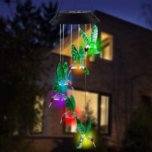 Colorful hummingbird-shaped solar LED wind chimes are illuminated at night, suspended outside a house.