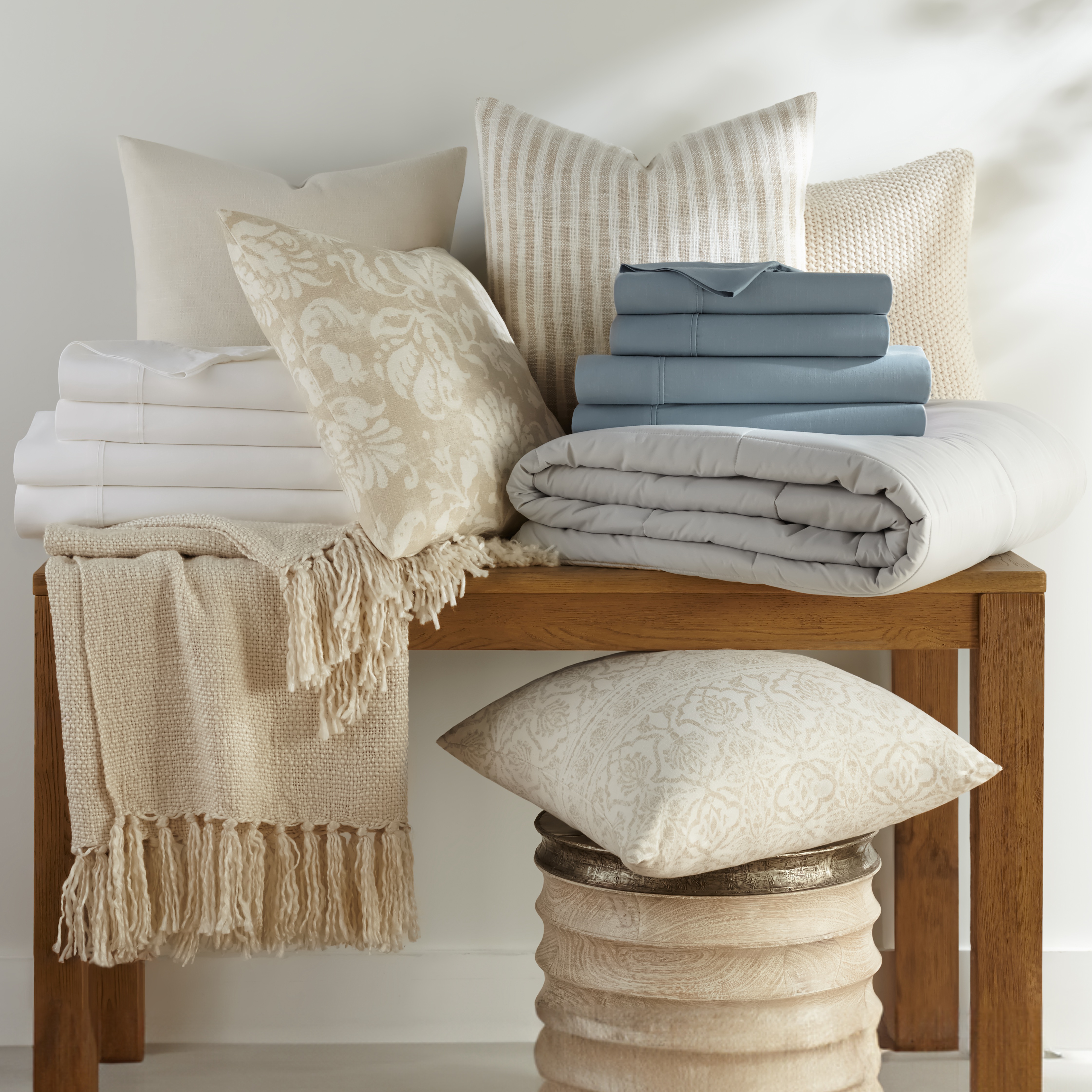 Assorted bedding items on a bench, including pillows, folded sheets, and a quilt.