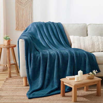 A blue plush throw is draped over a chair with a wooden side table nearby, featuring candles and a small vase with flowers.