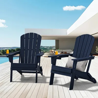 Two navy blue Adirondack chairs are placed on a wooden deck overlooking a modern patio, with drinks on the armrests.