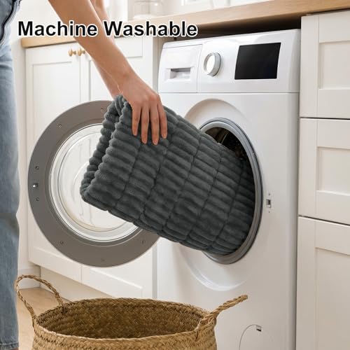 A person is placing a dark gray, quilted, machine-washable item into a front-loading washing machine. A woven basket is nearby.