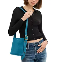 A person is wearing a ribbed black cardigan and blue jeans, carrying a small turquoise shoulder bag with a gold buckle detail.