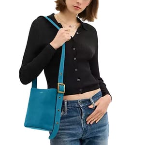 A person is wearing a ribbed black cardigan and blue jeans, carrying a small turquoise shoulder bag with a gold buckle detail.