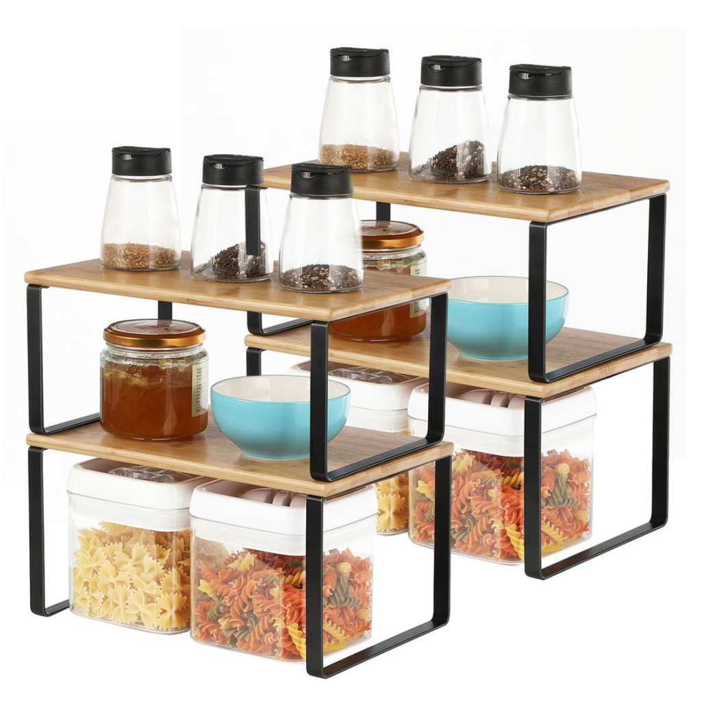 Set of four tiered kitchen counter shelves with black metal frames and wooden surfaces, displaying spice jars, honey jars, bowls, and containers filled with pasta.