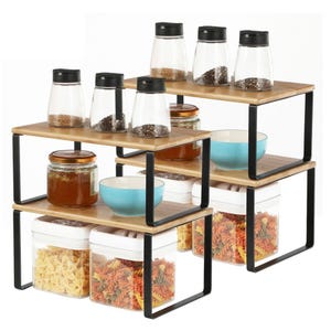 Set of four tiered kitchen counter shelves with black metal frames and wooden surfaces, displaying spice jars, honey jars, bowls, and containers filled with pasta.