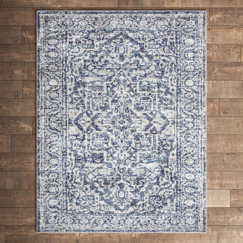 A blue and white patterned area rug featuring an intricate, vintage-inspired design is displayed on a wooden floor.