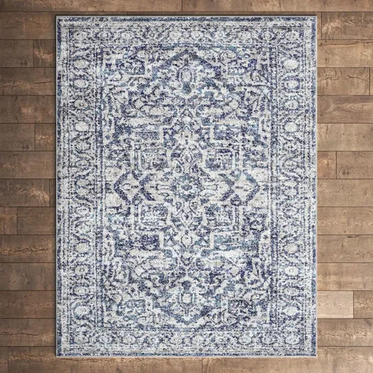 A blue and white patterned area rug featuring an intricate, vintage-inspired design is displayed on a wooden floor.