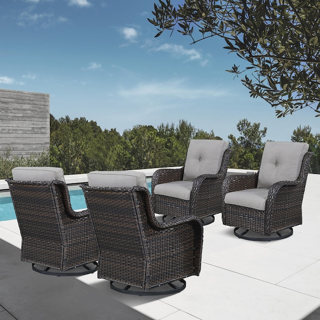 Four outdoor wicker swivel chairs with gray cushions are arranged on a patio by a pool, surrounded by greenery.
