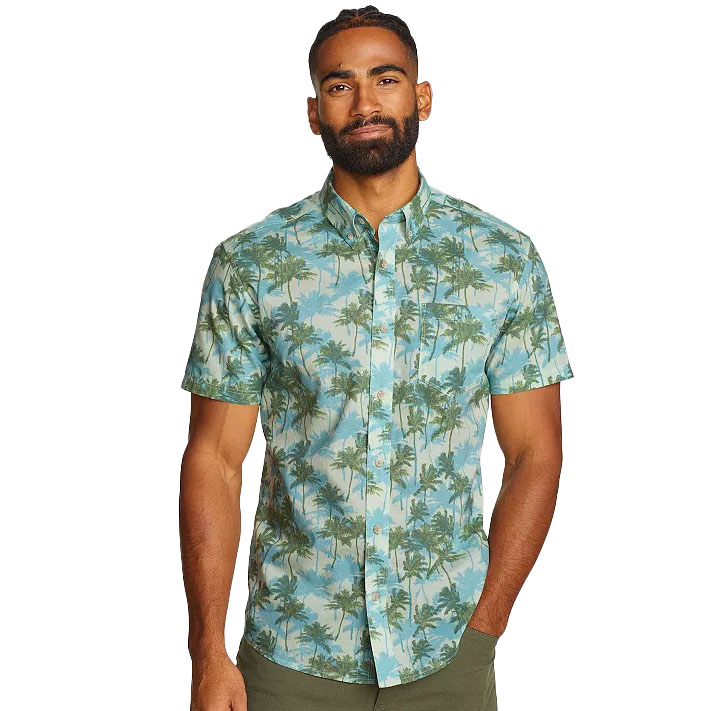 A man wears a short-sleeve button-up shirt with a green palm tree print on a light blue background, paired with olive-green pants.