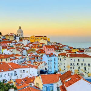 A picturesque view of Lisbon's historic buildings at sunset with the ocean in the background.