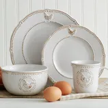 A rustic-style dinnerware set includes two plates, a bowl, and a mug, all featuring embossed chicken designs and dotted detailing. Brown eggs are placed nearby for decorative effect.