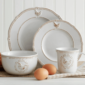 A rustic-style dinnerware set includes two plates, a bowl, and a mug, all featuring embossed chicken designs and dotted detailing. Brown eggs are placed nearby for decorative effect.