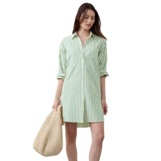 A woman is wearing a green and white striped shirt dress with rolled-up sleeves, and carrying a large woven bag.