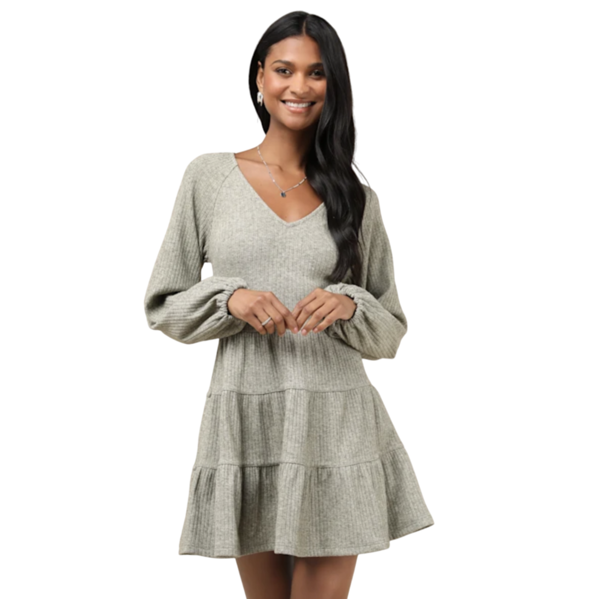 A woman is wearing a light gray, ribbed, long-sleeve, tiered mini dress with a V-neckline. She is accessorizing with a necklace and earrings.