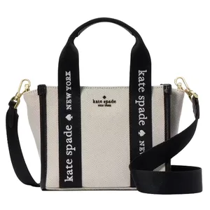A Kate Spade New York handbag with black and white canvas, featuring \“Kate Spade New York\“ text on the straps and gold hardware.