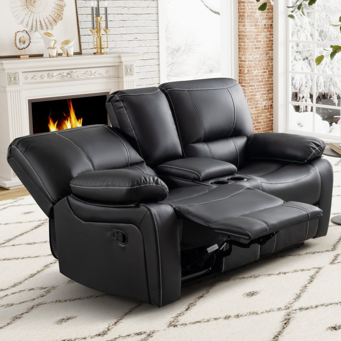 Black leather reclining loveseat with cup holders situated in a cozy living room featuring a fireplace and snowy window view.