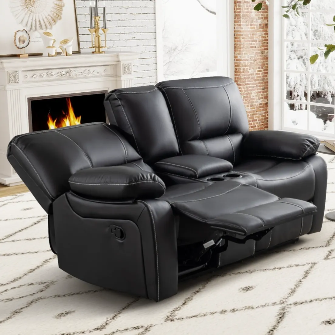Black leather reclining loveseat with cup holders situated in a cozy living room featuring a fireplace and snowy window view.