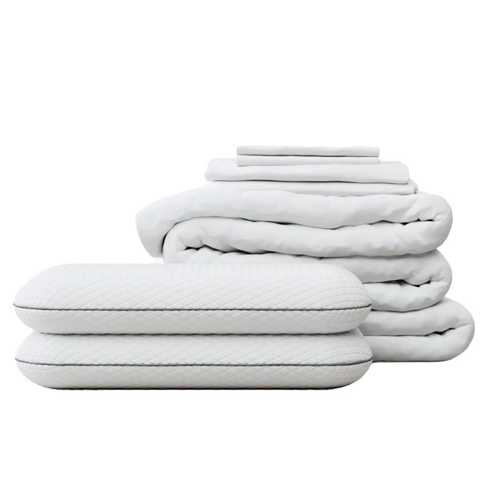 A set of white bedding items featuring a quilted texture, including two pillows, a folded blanket, and a stack of sheets.
