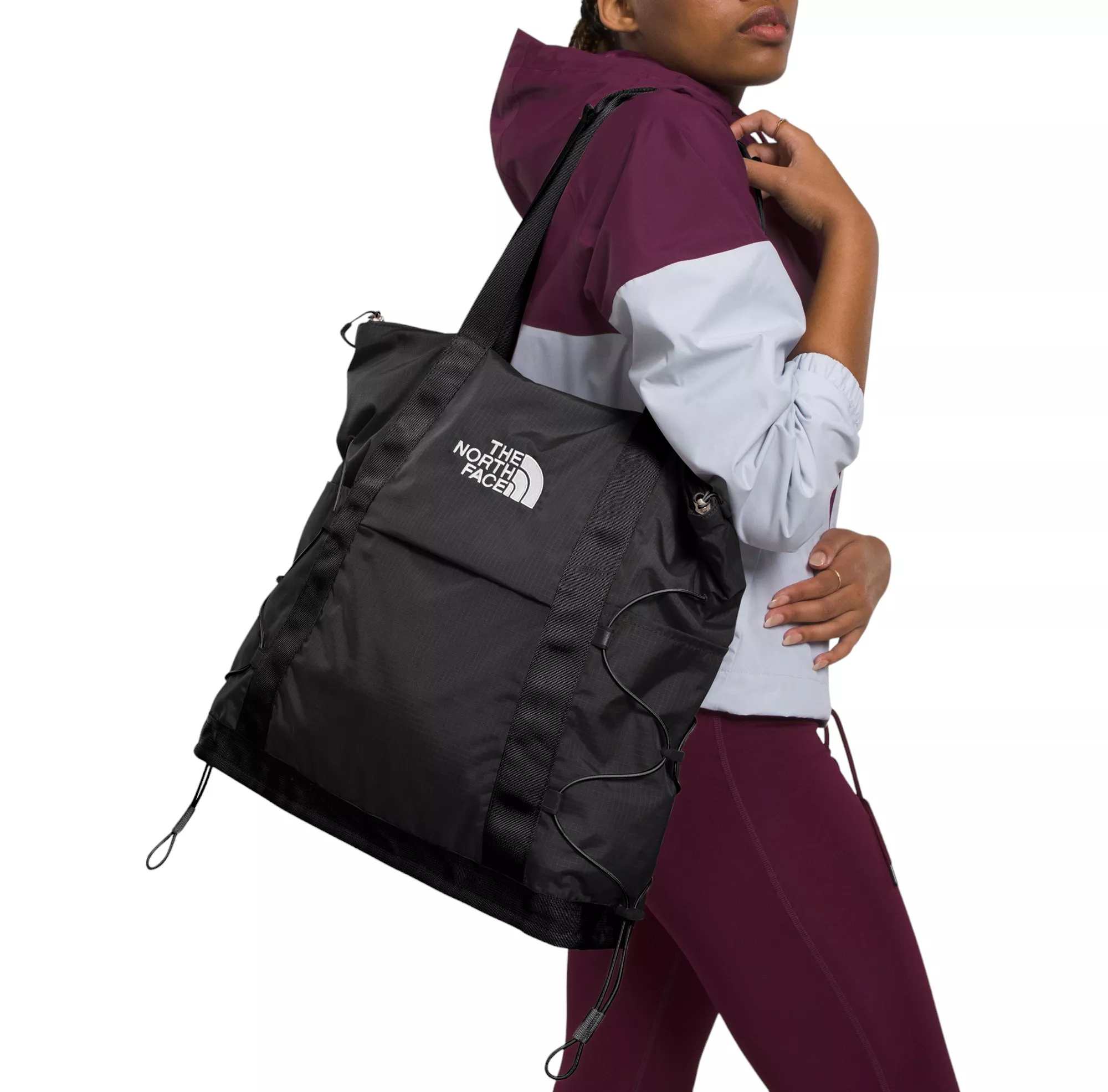 A person with a maroon and white jacket is carrying a black The North Face duffel bag on their shoulder.