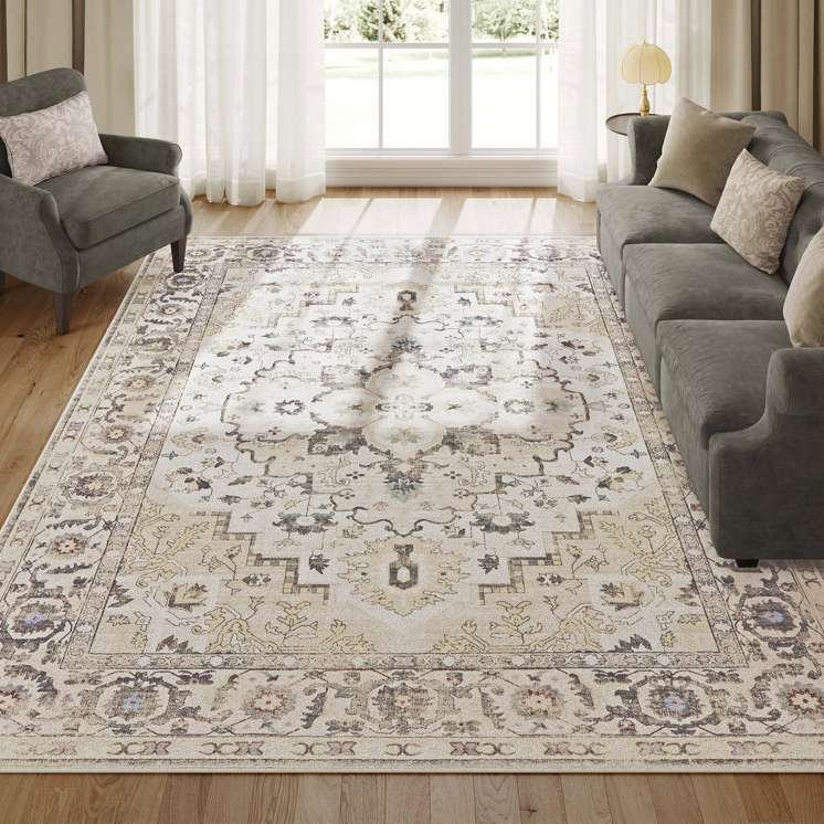 A traditional design 8' x 10' area rug featuring a central medallion with floral and geometric patterns in muted shades, surrounded by a detailed border; machine-washable with a soft texture, placed in a room with a gray sofa and an armchair.