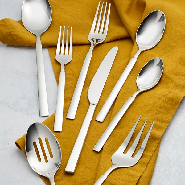 A set of shiny silver cutlery, including spoons, forks, and knives, is arranged on a mustard yellow cloth.