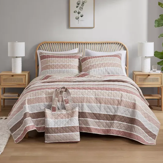 A cozy bedroom features a bed with a striped quilt and matching pillow shams, flanked by wooden nightstands and white lamps. A decorative wall art with botanical design hangs above, and a matching patterned tote bag rests on the bed.