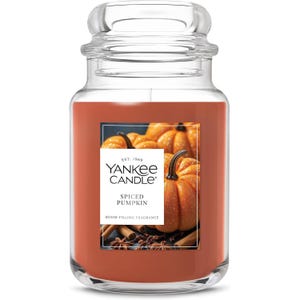 Yankee Candle featuring a Spiced Pumpkin scent in a clear jar, showcasing images of pumpkins and spices on the label.
