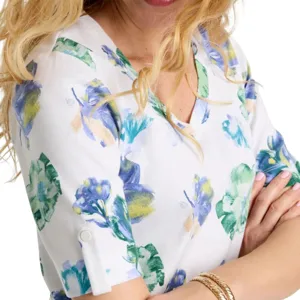 A white blouse with a floral pattern featuring shades of blue, green, and yellow, with rolled-up sleeves secured by a button detail. The person is also wearing gold bangles.