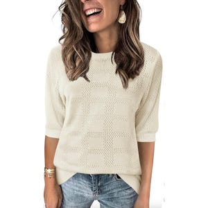 Women's short-sleeve ivory sweater features a knitted grid pattern with ribbed cuffs and hem, paired with light blue jeans and accessorized with gold earrings and bracelets.