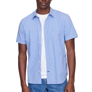 A man is wearing a light blue short-sleeve button-up shirt over a white T-shirt, paired with blue jeans.
