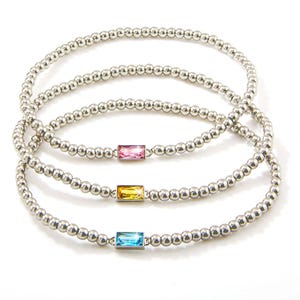 Three silver beaded stretch bracelets each featuring a rectangular gemstone: pink, yellow, and blue.